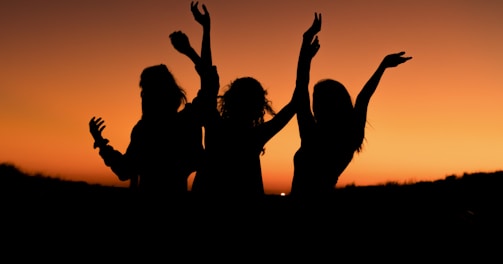 silhouette of three woman with hands on the air while dancing during sunset