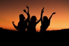 silhouette of three woman with hands on the air while dancing during sunset