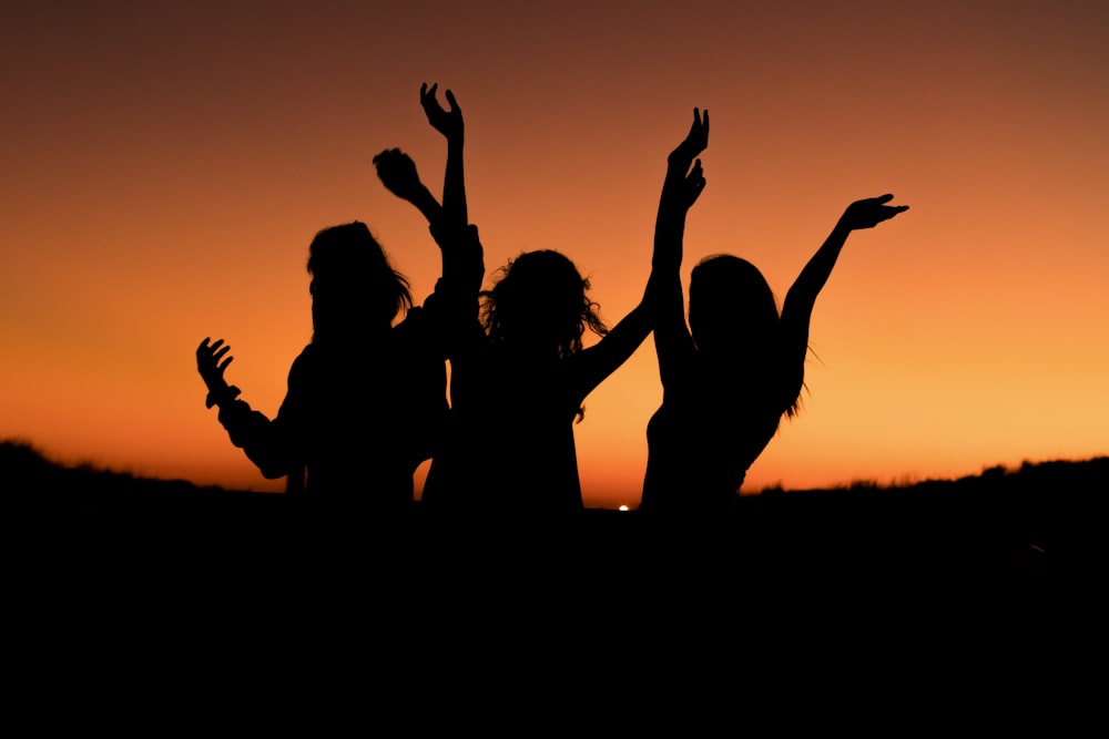 Silueta de tres mujeres con las manos en el aire mientras bailan durante la puesta del sol