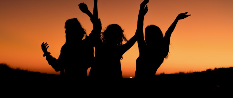 silhouette of three woman with hands on the air while dancing during sunset