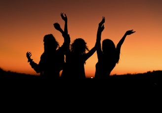silhouette of three woman with hands on the air while dancing during sunset