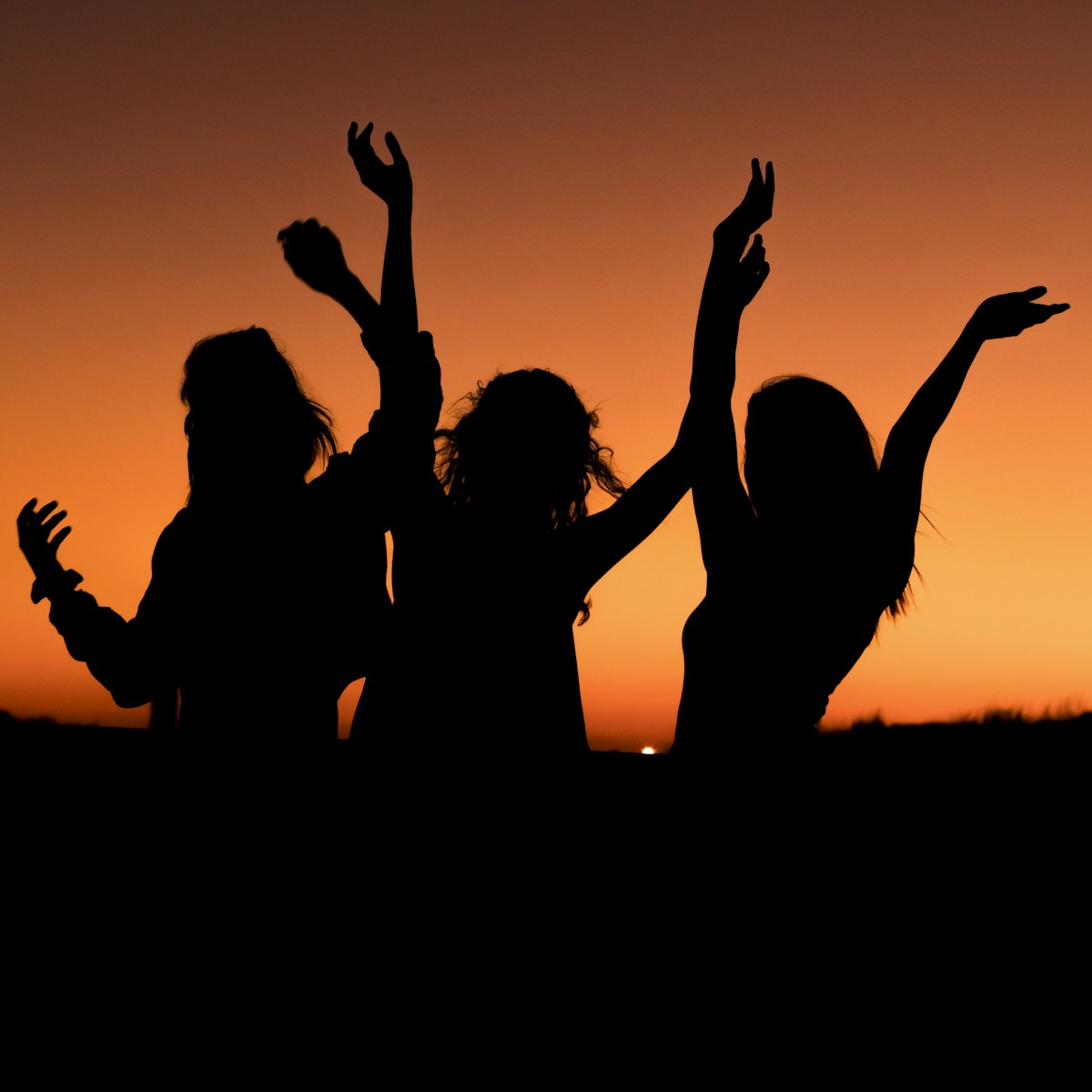 silhouette of three woman with hands on the air while dancing during sunset