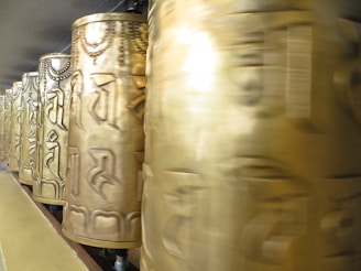 A row of golden prayer wheels adorned with intricate patterns and symbols spins in unison, creating a sense of motion and spirituality.