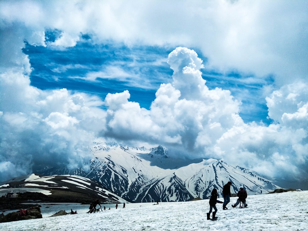 personnes debout sur un sol enneigé près des montagnes pendant la journée