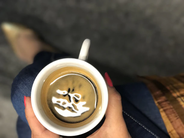 Close-up of a woman’s hand holding a coffee cup, showcasing a stylish striped casual top sleeve.
