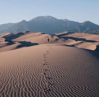 person walking on sand dunes leaving footprint trails behind