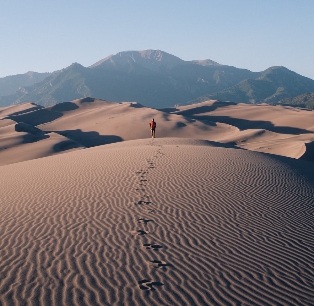 person walking on sand dunes leaving footprint trails behind