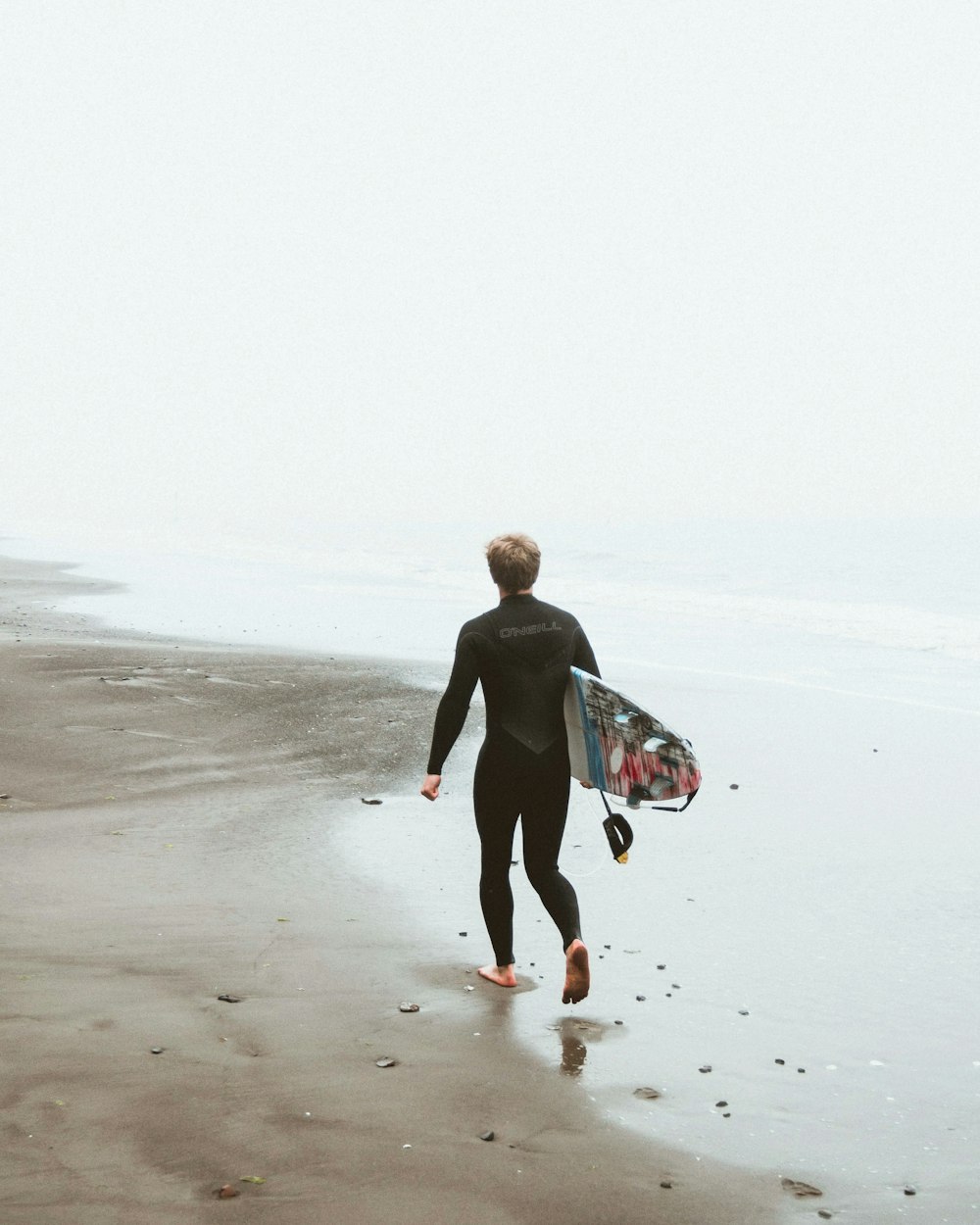 man walking on the beach carrying surfboard