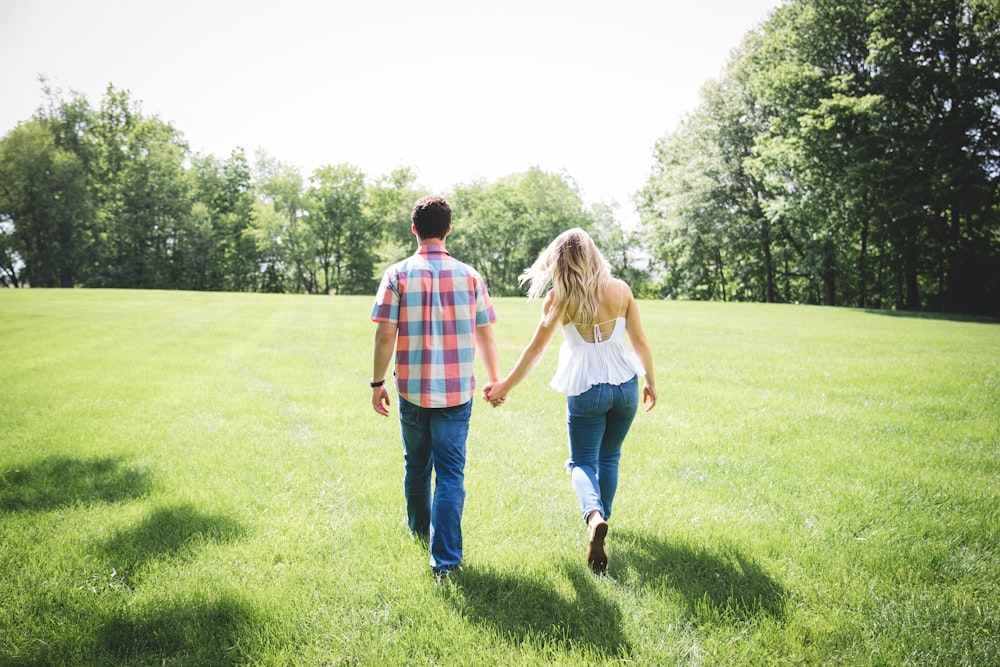 hombre y mujer caminando en un campo de hierba verde rodeado de árboles