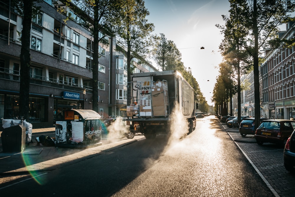 camion se déplaçant sur une route en béton gris entre les arbres