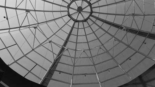 A geometric glass dome structure with a central circular opening, featuring numerous triangular glass panels supported by metal beams.
