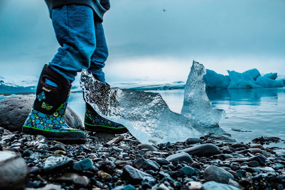 Persona in piedi sulle rocce accanto all'iceberg e al mare durante il giorno