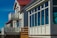 A row of modern homes with large windows and small balconies. The buildings showcase a clean architectural design with white and red detailing. The sky is clear and blue, illuminating the facade of the houses.