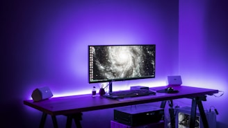 A minimalist workspace with a sleek computer displaying vibrant 3D graphics in cyan and purple hues.