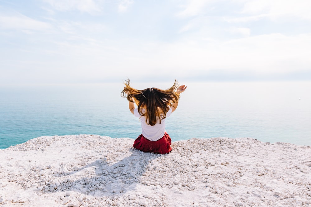 woman sitting on cliff near body of water