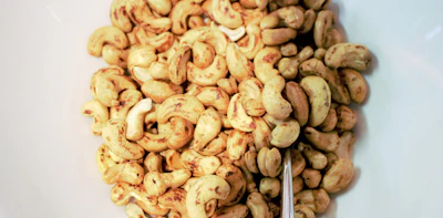 Close-up of golden roasted cashew nuts spilling from a rustic wooden bowl on a warm-toned background.