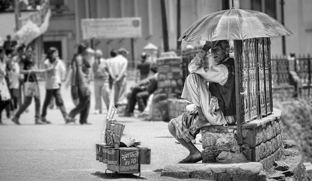 grayscale photo of man sitting on concrete bench