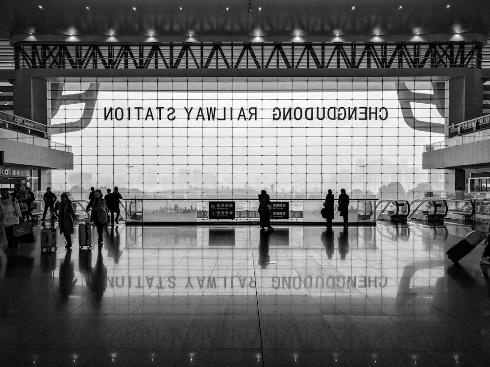 Schwarz-Weiß-Aufnahme des Bahnhofsfoyers mit Menschen und großem Fenster und Spiegelung auf dem Boden