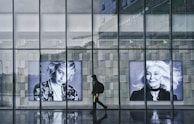 A model in a tailored black and white ensemble walking past a modern glass building with reflections.