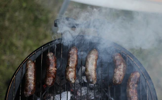 Close-up of sizzling Carolina sausage links topped with grilled onions and peppers on a rustic grill.