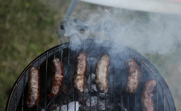Close-up of sizzling Carolina sausage links topped with onions and peppers on a rustic grill.