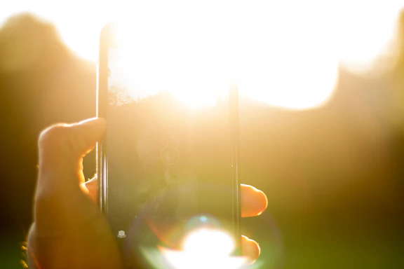 A warm, inviting photo of a senior smiling while using a smartphone with gentle sunlight in the background.