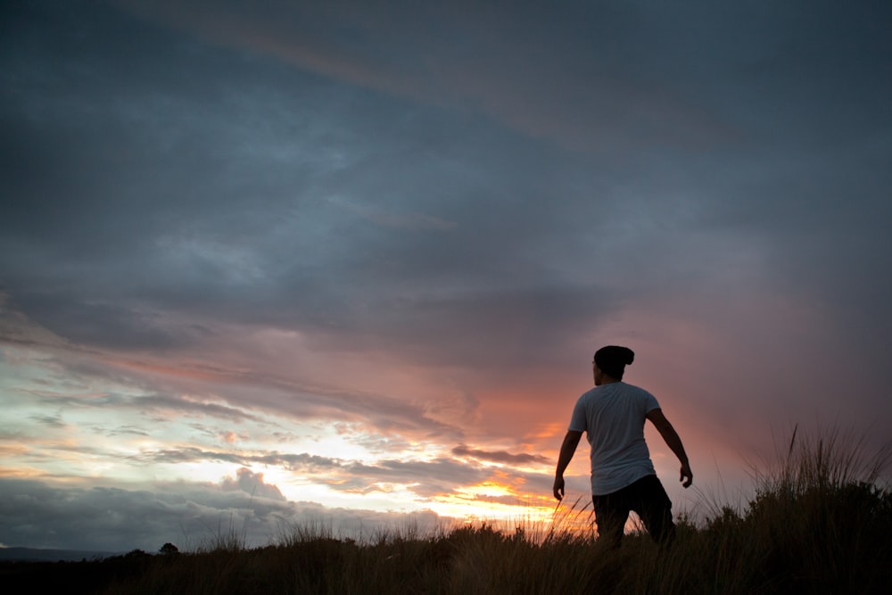 man standing on grass under white clouds