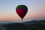 A colorful hot air balloon floating above rolling green hills at dawn
