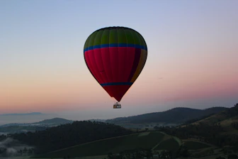 Colorful hot air balloon floating over lush green hills at sunrise