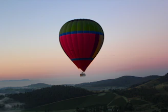 A colorful hot air balloon lifting off at sunrise over a lush green valley