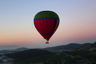 A colorful hot air balloon floating over rolling hills at dawn.