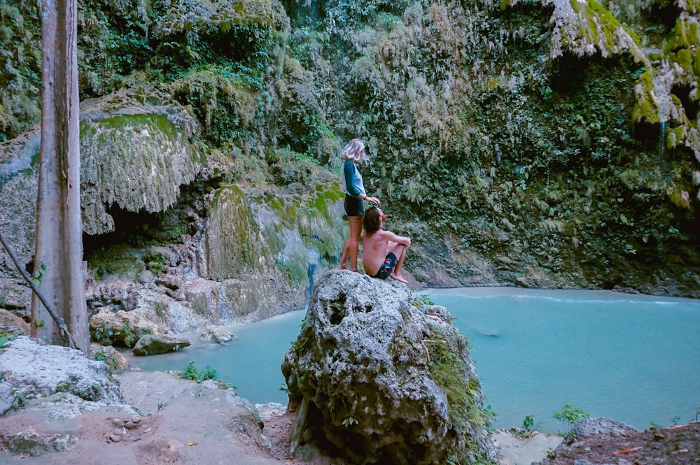 woman standing behind man sitting on rock boulder