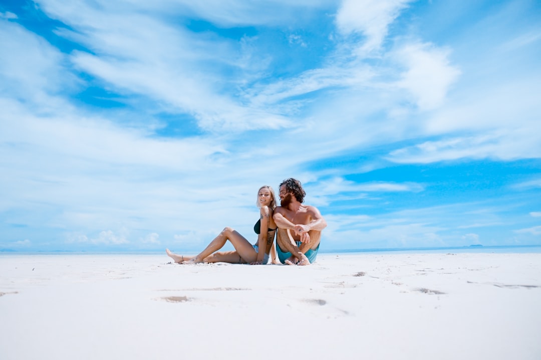 man sitting beside of woman in black bikini top, Young couple on an empty beach