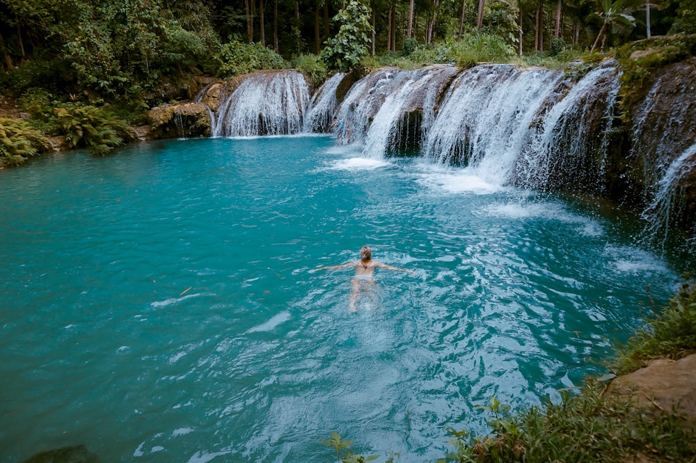 a person swimming in a pool next to a waterfall