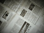 A close-up of a newspaper with multiple pages spread out. The text is written in a non-Latin script, possibly Chinese. There are also images within the articles, including one with the word 'NEWS'. The pages are slightly overlapping, creating an organized yet informal layout.