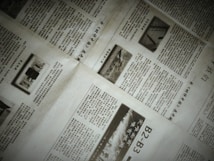 A close-up of a newspaper with multiple pages spread out. The text is written in a non-Latin script, possibly Chinese. There are also images within the articles, including one with the word 'NEWS'. The pages are slightly overlapping, creating an organized yet informal layout.