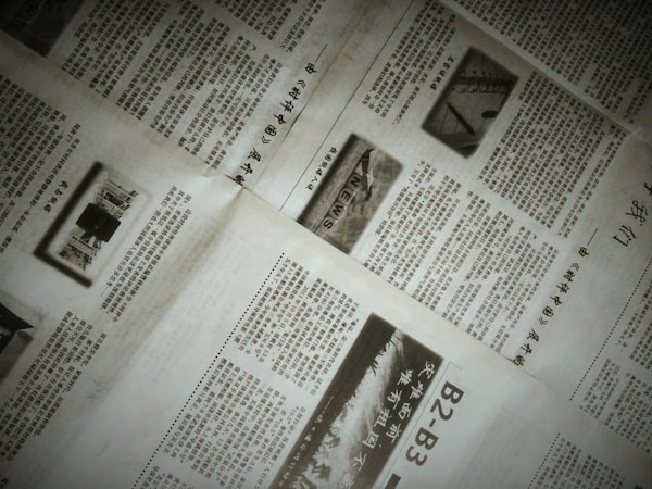 A close-up of a newspaper with multiple pages spread out. The text is written in a non-Latin script, possibly Chinese. There are also images within the articles, including one with the word 'NEWS'. The pages are slightly overlapping, creating an organized yet informal layout.