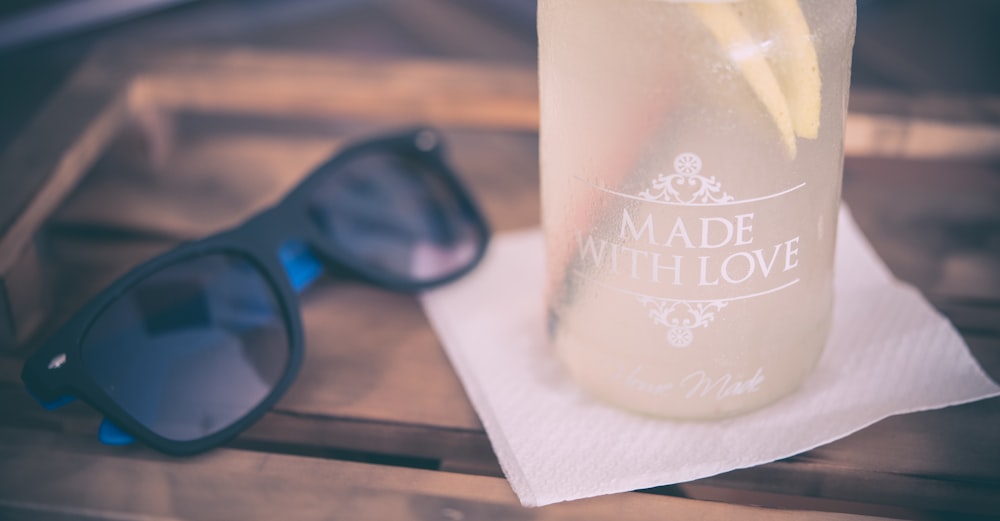 occhiali da sole con cornice nera accanto alla bottiglia di vetro sul tavolo