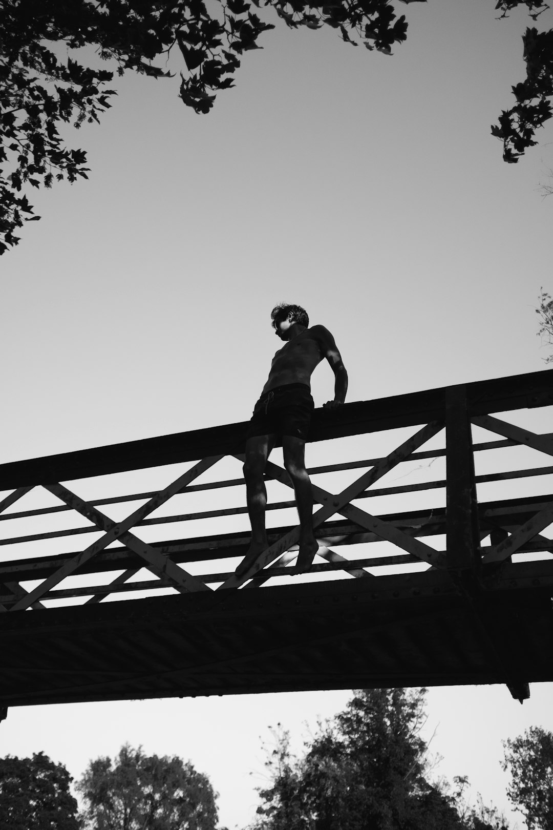 grayscale photography of man sitting on edge of bridge