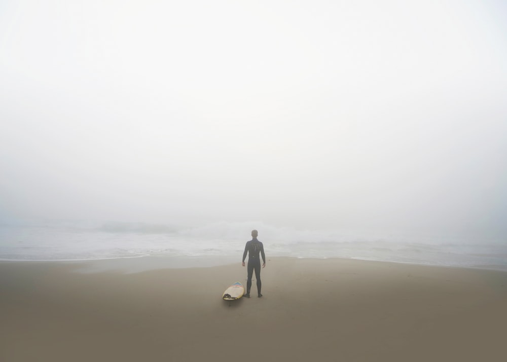 man standing beside surfboard on seashore