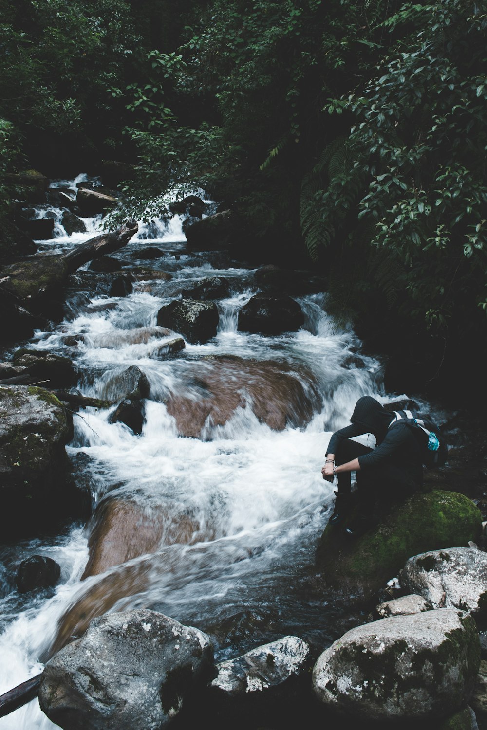 Persona con sudadera con capucha negra sentada junto a cascadas