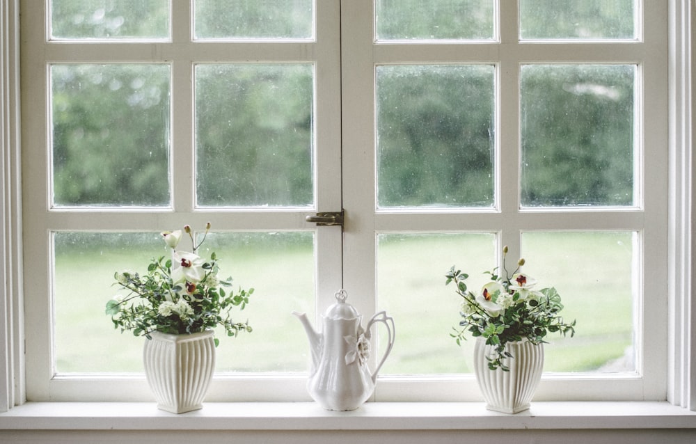 Tetera blanca y jarrones de flores en el cristal de la ventana