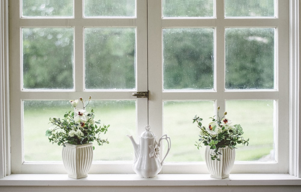 bule branco e vasos de flores de reboque na vidraça