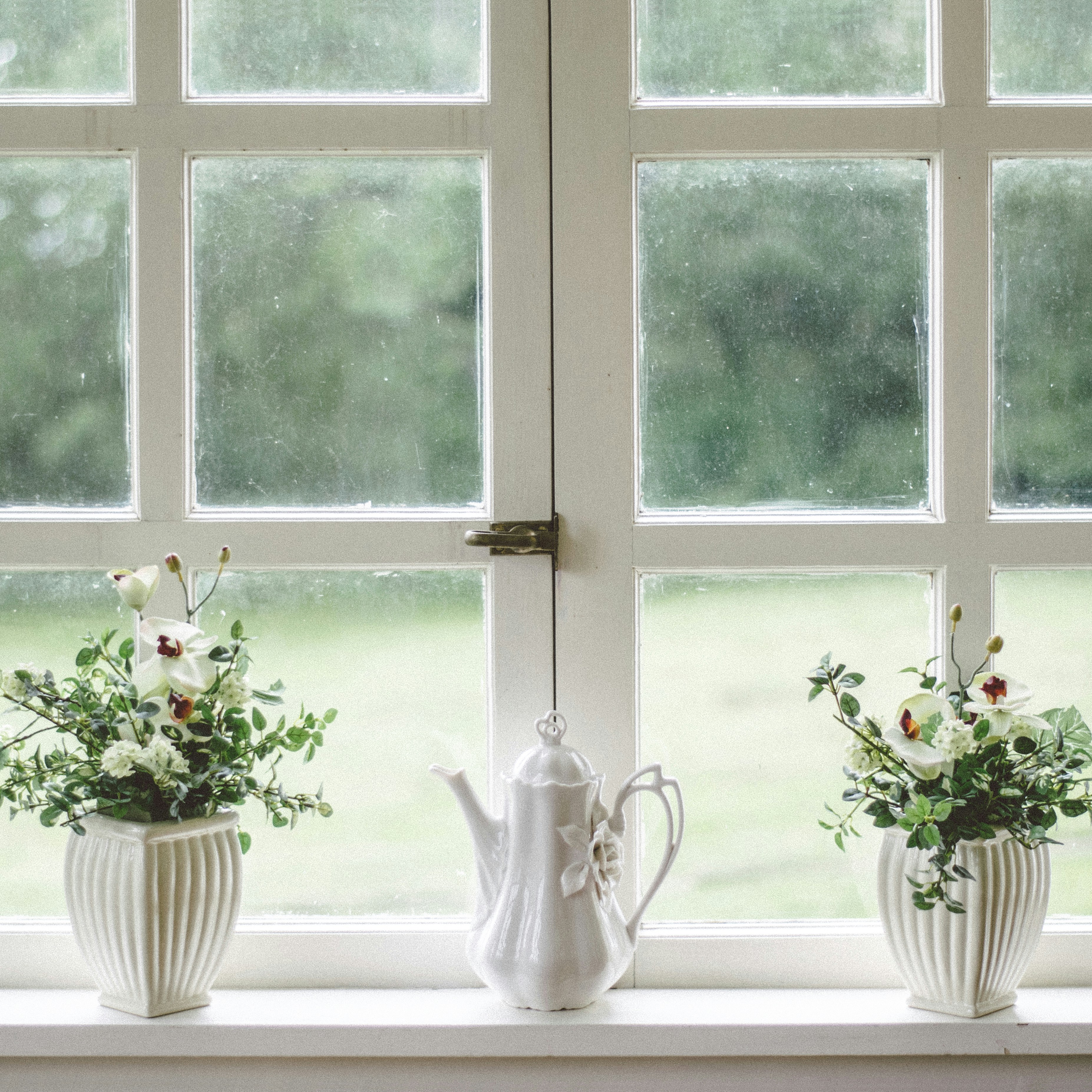 white teapot and tow flower vases on windowpane