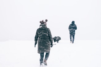 photo of two person wearing black jacket walking on snowy weather