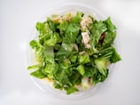 A fresh salad consisting of leafy green lettuce, pieces of cooked chicken, and possibly other vegetables or toppings, in a transparent bowl. The colors and textures suggest crispness and freshness.