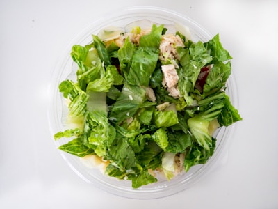 A fresh salad consisting of leafy green lettuce, pieces of cooked chicken, and possibly other vegetables or toppings, in a transparent bowl. The colors and textures suggest crispness and freshness.