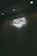 A neon sign depicting a handshake is mounted on a dark wall, illuminated by overhead lights.