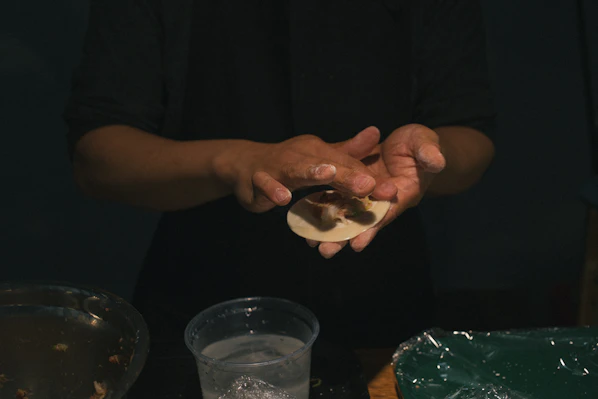 A close-up of hands carefully shaping traditional Indian sweets in a rustic kitchen setting.