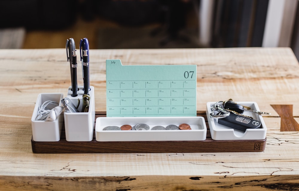 Image shows a desk with a calendar, keys, earphones and some coins on top in an organiser.
